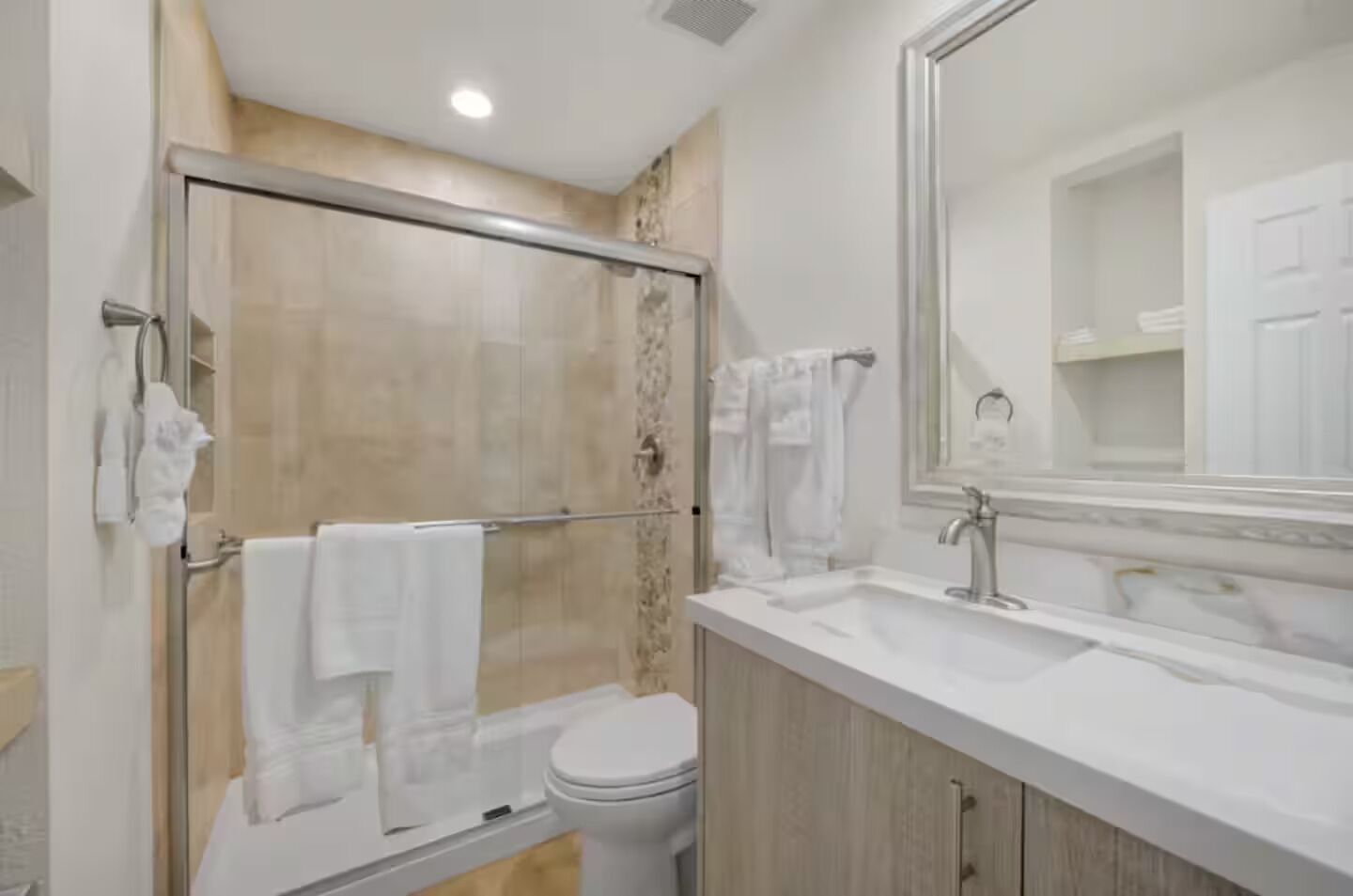 A modern bathroom with a glass shower enclosure, a white toilet, and a large mirror above a sink.