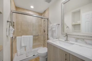 Un baño moderno con cabina de ducha de vidrio, un inodoro blanco y un espejo grande sobre un lavabo.
