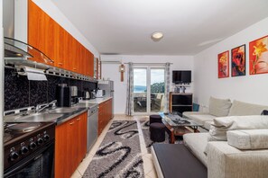 Eine moderne Küche mit Herd, Spüle und Holzschränken, ein Essbereich mit Tisch und Stühlen sowie ein Wohnzimmer mit Sofa und Kunstwerken.