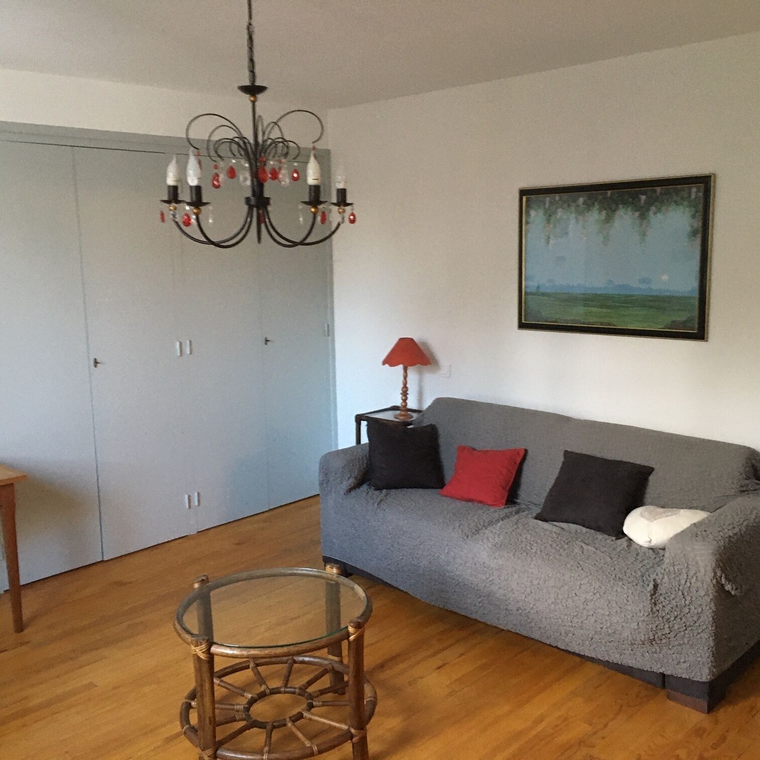Un salon avec un canapé gris, une table basse en verre, un plancher en bois, un lustre et un tableau accroché au mur.