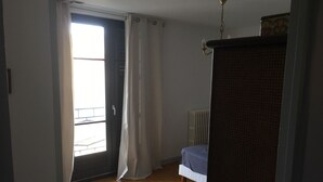 Makuuhuoneessa on puulattia, patteri, sinisellä päällisellä varustettu sänky ja ikkuna, jossa on verhot.