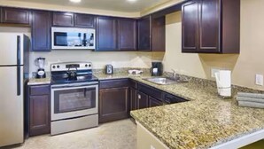 Una cocina con armarios de madera oscura, un refrigerador de acero inoxidable, horno empotrado, microondas, encimeras de granito y un lavamanos.