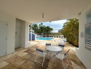 Ein Poolbereich mit Tisch und Stühlen, einem Pool und Blick auf ein Gebäude sowie Palmen.