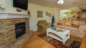 Un salon avec une cheminée, un téléviseur, un ventilateur de plafond et un canapé.