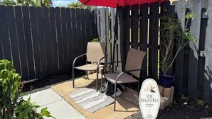 A patio with a red umbrella, two chairs, a small table, and a sign for 'The Magnolia Retreat.' - Quiet studio w private outdoor area close to major amenities (Sunrise)