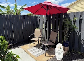 A patio with a red umbrella, two chairs, a small table, and a sign for 'The Magnolia Retreat.' - Quiet studio w private outdoor area close to major amenities (Sunrise)
