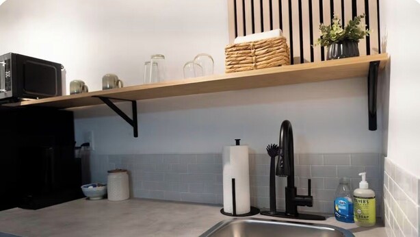 A kitchen with a stainless steel sink, a microwave, a toaster, and a shelf with towels and a plant. - Quiet studio w private outdoor area close to major amenities (Sunrise)