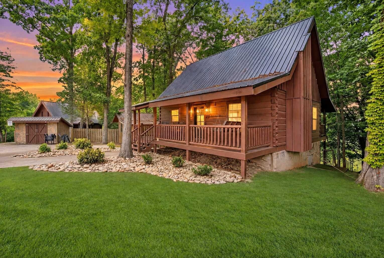 Un chalet rustique doté d’un porche, entouré d’une pelouse bien entretenue et d’arbres.