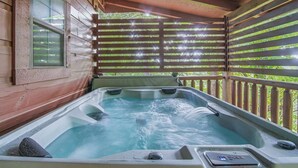 Un espace avec un jacuzzi, une terrasse en bois, une fenêtre et une vue sur la verdure.
