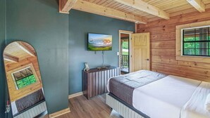 Une chambre à coucher avec un lit, un téléviseur fixé au mur, un plafond en bois et une porte donnant sur un espace extérieur.