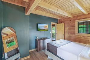 Ein Schlafzimmer mit einem Bett, einem an der Wand montierten Fernseher, einer Holzbalkendecke und einer Tür zu einem Außenbereich.