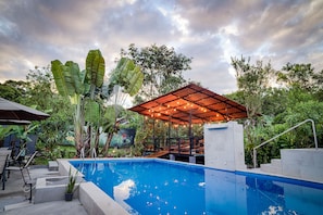 Una piscina con cubierta de madera, rodeada de exuberante vegetación y un área de estar techada.