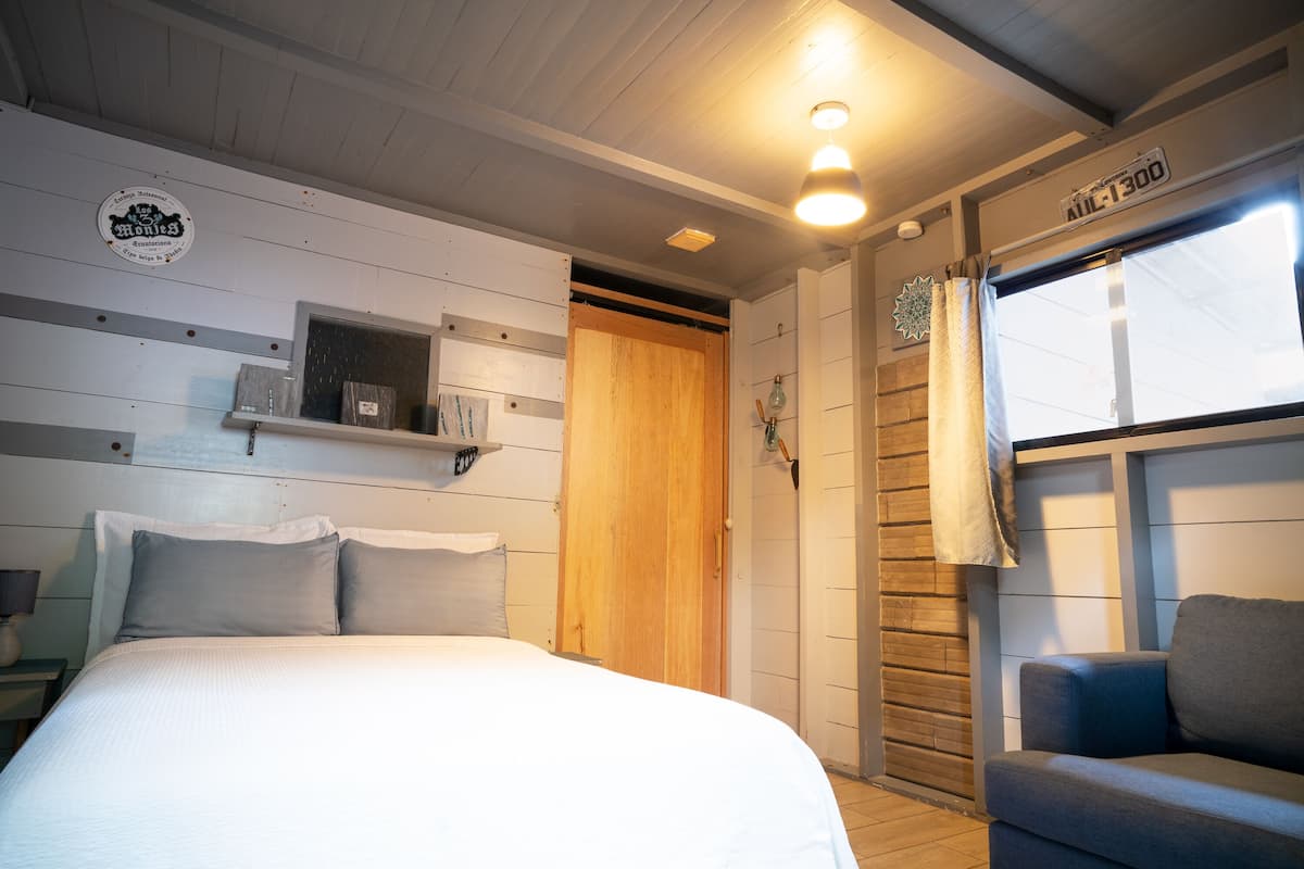 A bedroom with a bed, a nightstand, a wooden door, a window with curtains, and a sign on the wall.