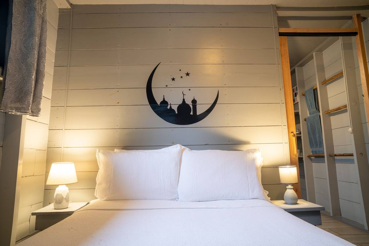 A bed with white linens, two bedside lamps, and a wall-mounted crescent moon decoration with stars.