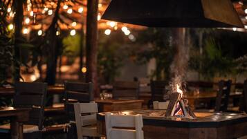 Ein Restaurant mit Holztischen und -stühlen, einem zentralen Kamin und Lichterketten im Hintergrund.