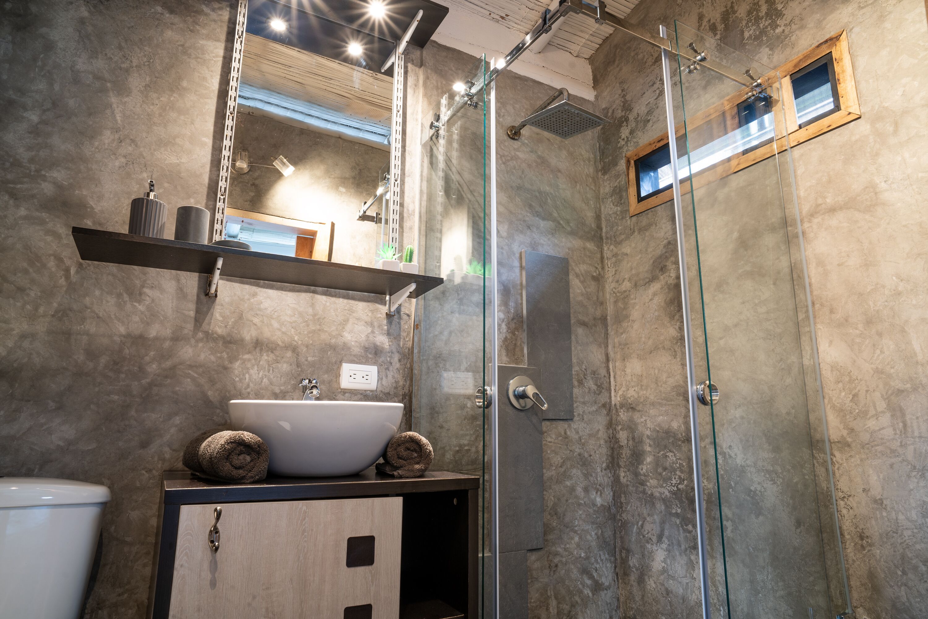 A modern bathroom with a glass shower enclosure, a wooden vanity with a sink, and a towel on the counter.