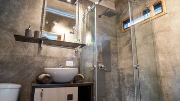 A modern bathroom with a glass shower enclosure, a wooden vanity with a sink, and a towel on the counter.