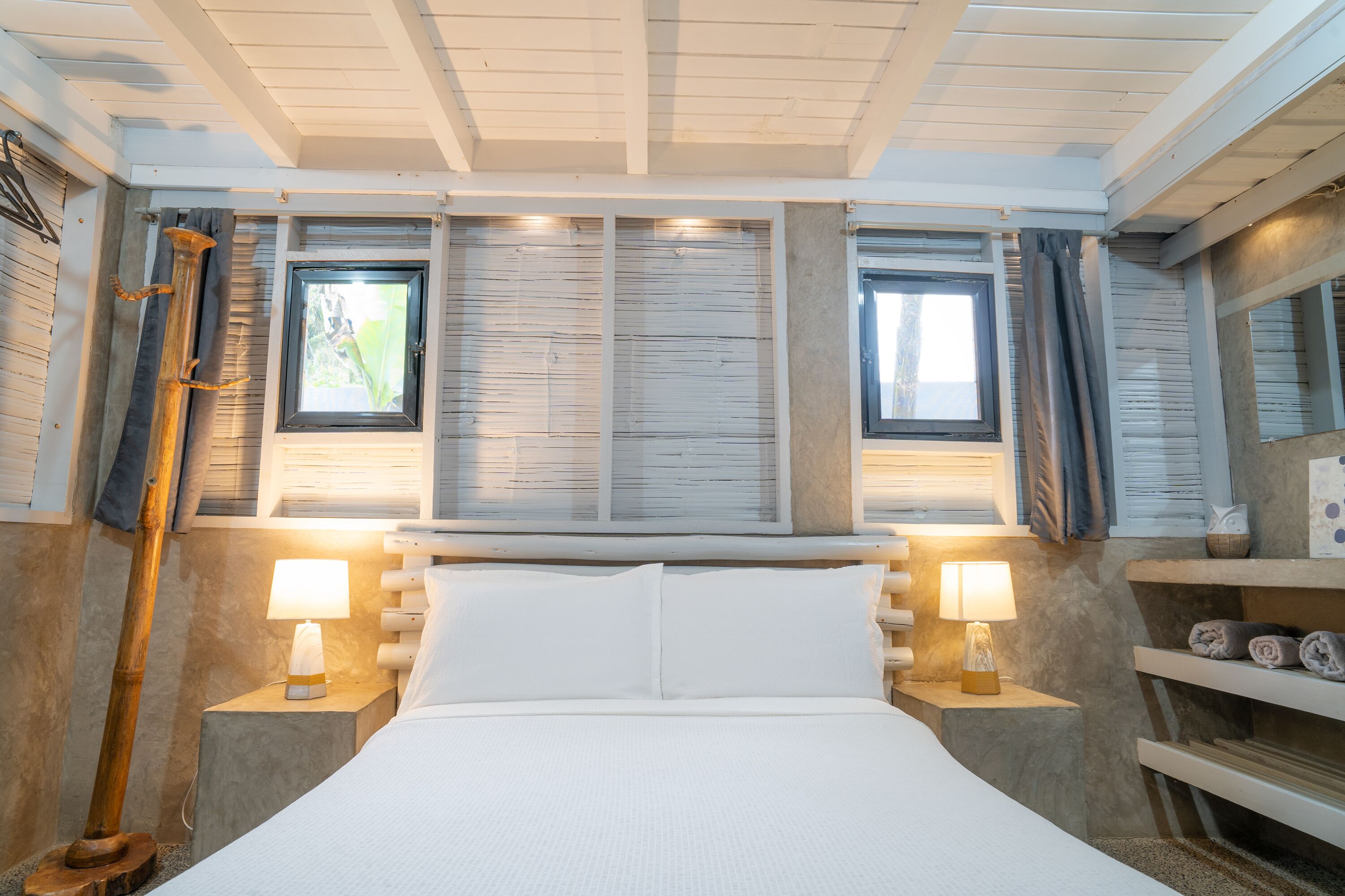 A bedroom with a bed, two bedside lamps, a window, and a shelf with towels.