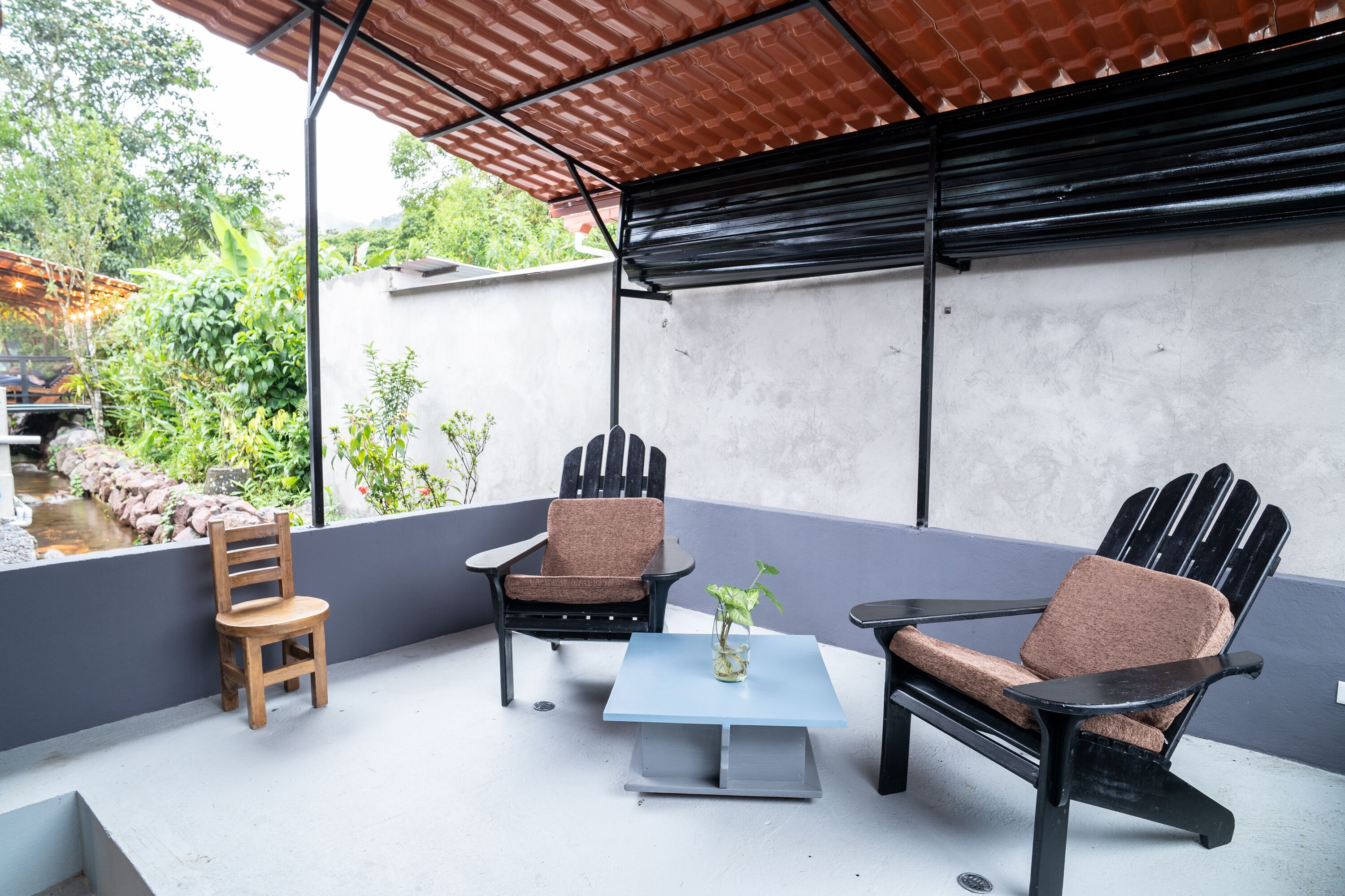 A patio with two Adirondack chairs, a wooden chair, and a small table with a vase.