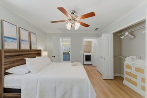 Ein Schlafzimmer mit Bett, Deckenventilator, Kommode und begehbarem Kleiderschrank.