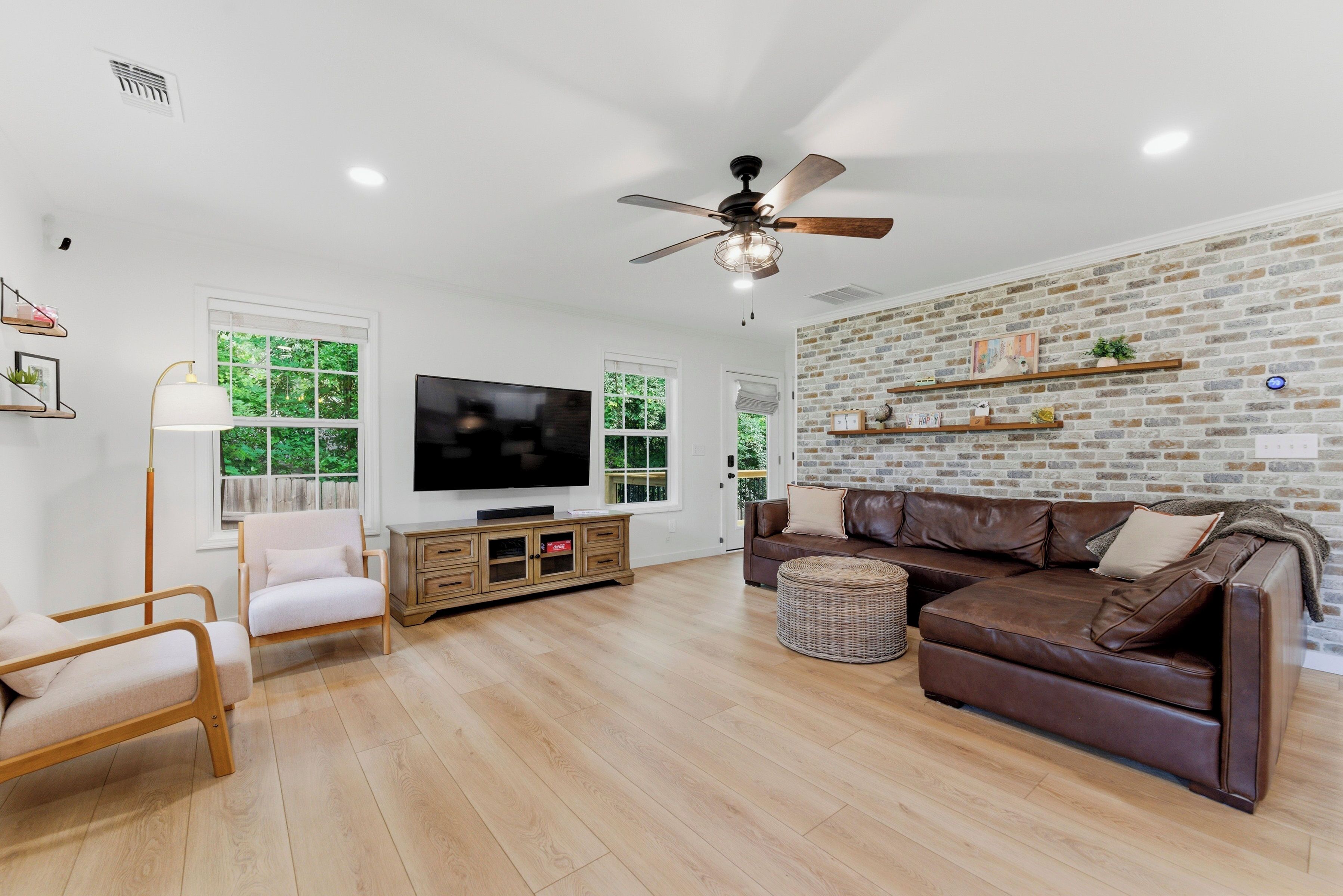 A modern living room with a flat-screen TV, a brown leather sofa, a wooden coffee table, and a ceiling fan.