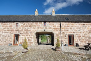 A stone building with a central archway, stone walls, and a cobblestone ground. - Jersey Cottage at The Dairy at Daviot (Inverness)
