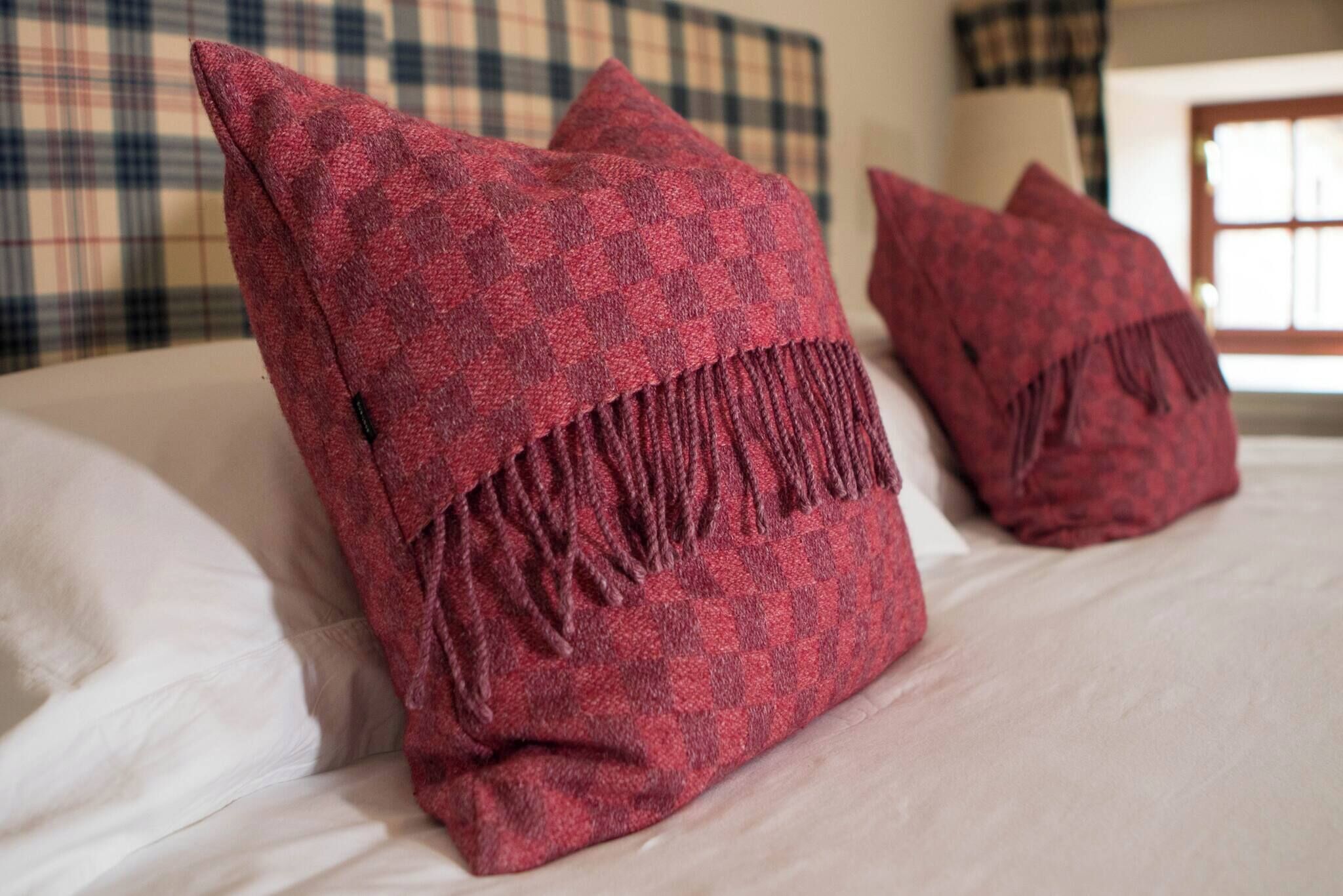 A bed with red pillows and a plaid headboard.