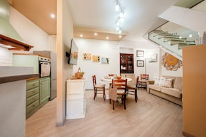 Una cocina moderna con comedor, armarios de madera, horno empotrado y una escalera que sube a un nivel superior.