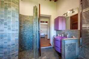 A bathroom with a glass shower enclosure, a purple vanity, and a wooden door.