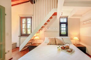 A bedroom with a bed, a staircase, two windows, a radiator, and a tray of breakfast.