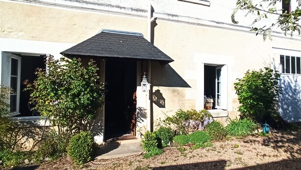 A building with a dark roof, a small porch, and a garden with various plants.