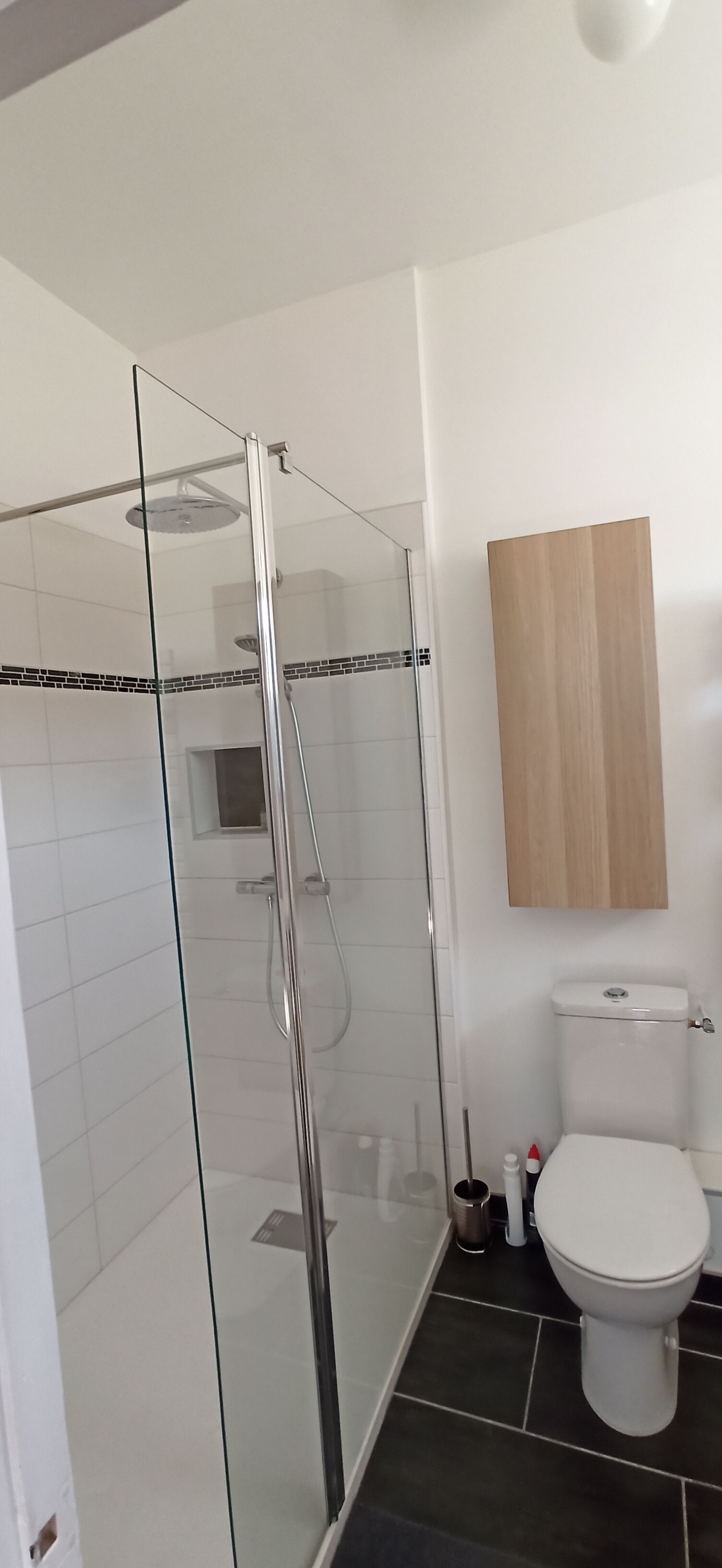 Un baño moderno con ducha de vidrio, inodoro y gabinete de madera sobre el inodoro.