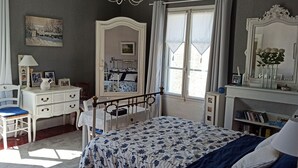 A bedroom with a bed, a dresser, a chair, a window with curtains, a mirror, and a bookshelf.