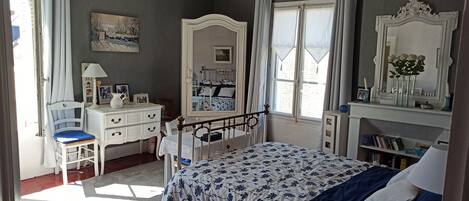 A bedroom with a bed, a dresser, a chair, a window with curtains, a mirror, and a bookshelf.