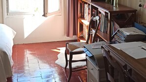 A room with a bed, a desk with papers, a bookshelf, and a window with curtains.