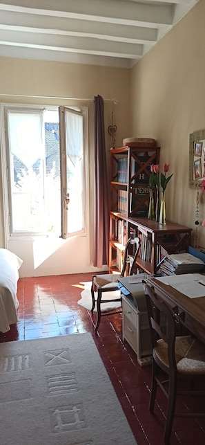 Une pièce comprenant un lit, un bureau avec des papiers, une bibliothèque et une fenêtre avec des rideaux.