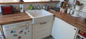 Une cuisine avec un évier blanc, un plan de travail en bois et un appareil de la marque Brandt.