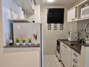Eine kleine Küche mit Mikrowelle, Toaster und Spüle. Auf der Arbeitsplatte stehen Blumentöpfe und über der Spüle befindet sich ein kleines Fenster.