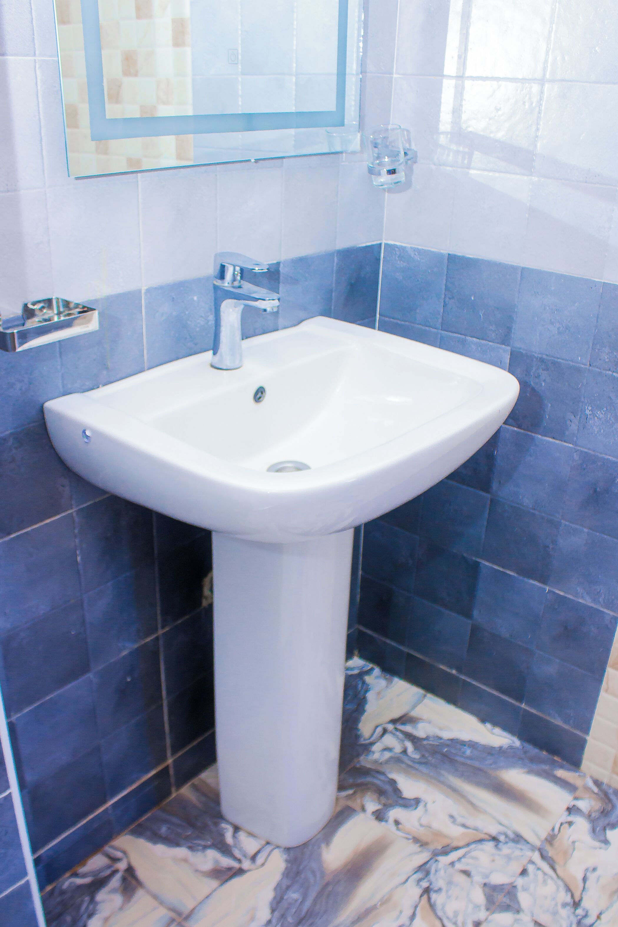 Un baño con un lavamanos blanco pedestal, paredes con azulejos azules y blancos, y un piso con diseño de mármol.