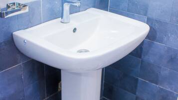 Un baño con un lavamanos blanco pedestal, paredes con azulejos azules y blancos, y un piso con diseño de mármol.