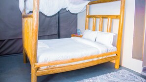 Una cama con dosel, ropa de cama blanca, estructura de madera y una mesita de noche con una botella de agua.