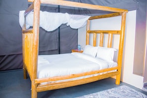 A four-poster bed with white linens, a wooden frame, and a nightstand with a water bottle.