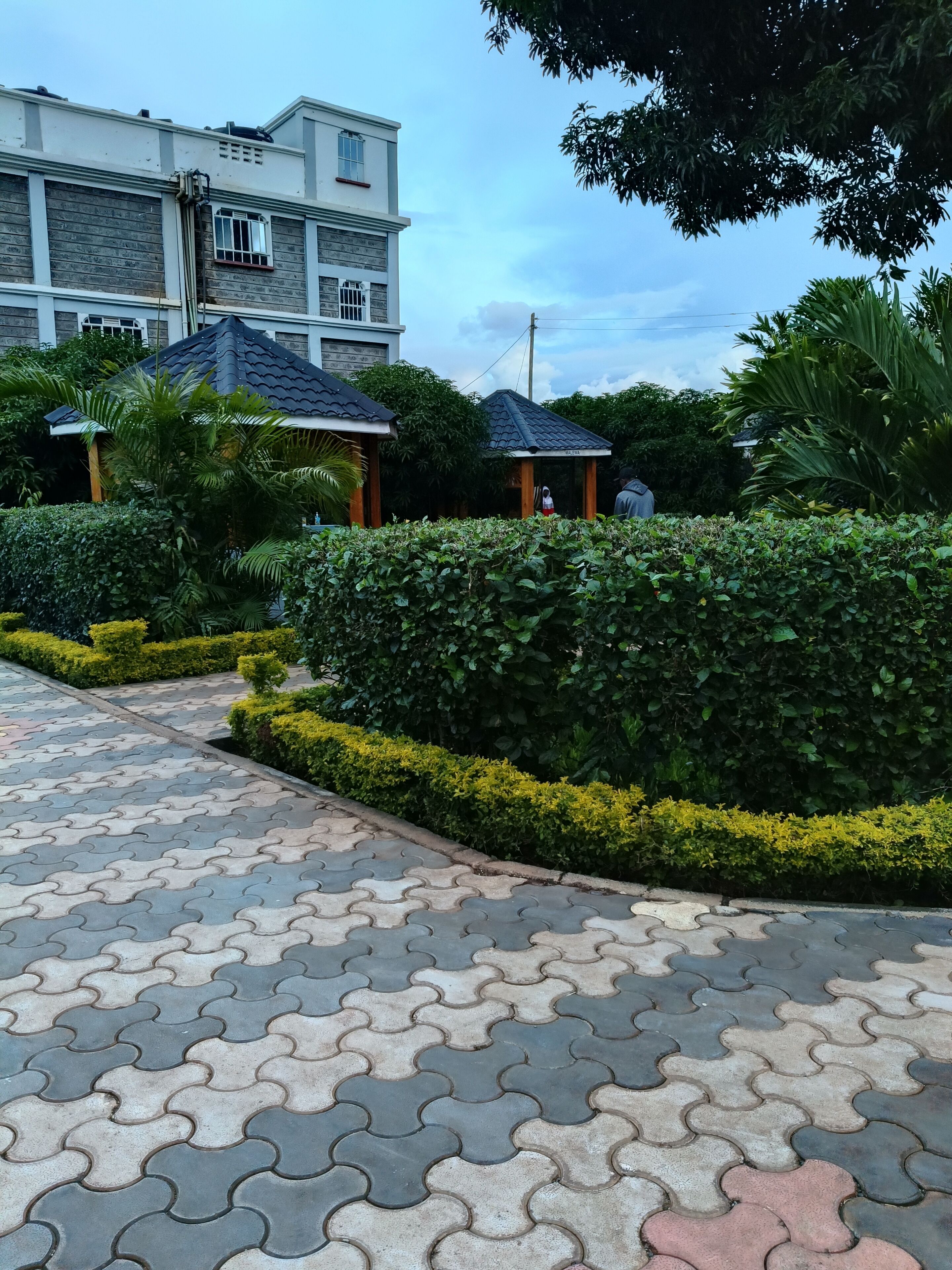 A paved pathway leading to a building with a tiled roof and a covered area.