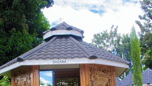 Una edificación de estilo pabellón con techo de tejas, con el nombre 'SAGANA', rodeada de exuberante follaje.