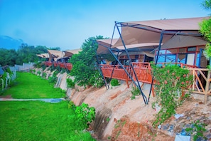 A series of outdoor structures with elevated platforms and attached canopies, surrounded by greenery and a sloped landscape.