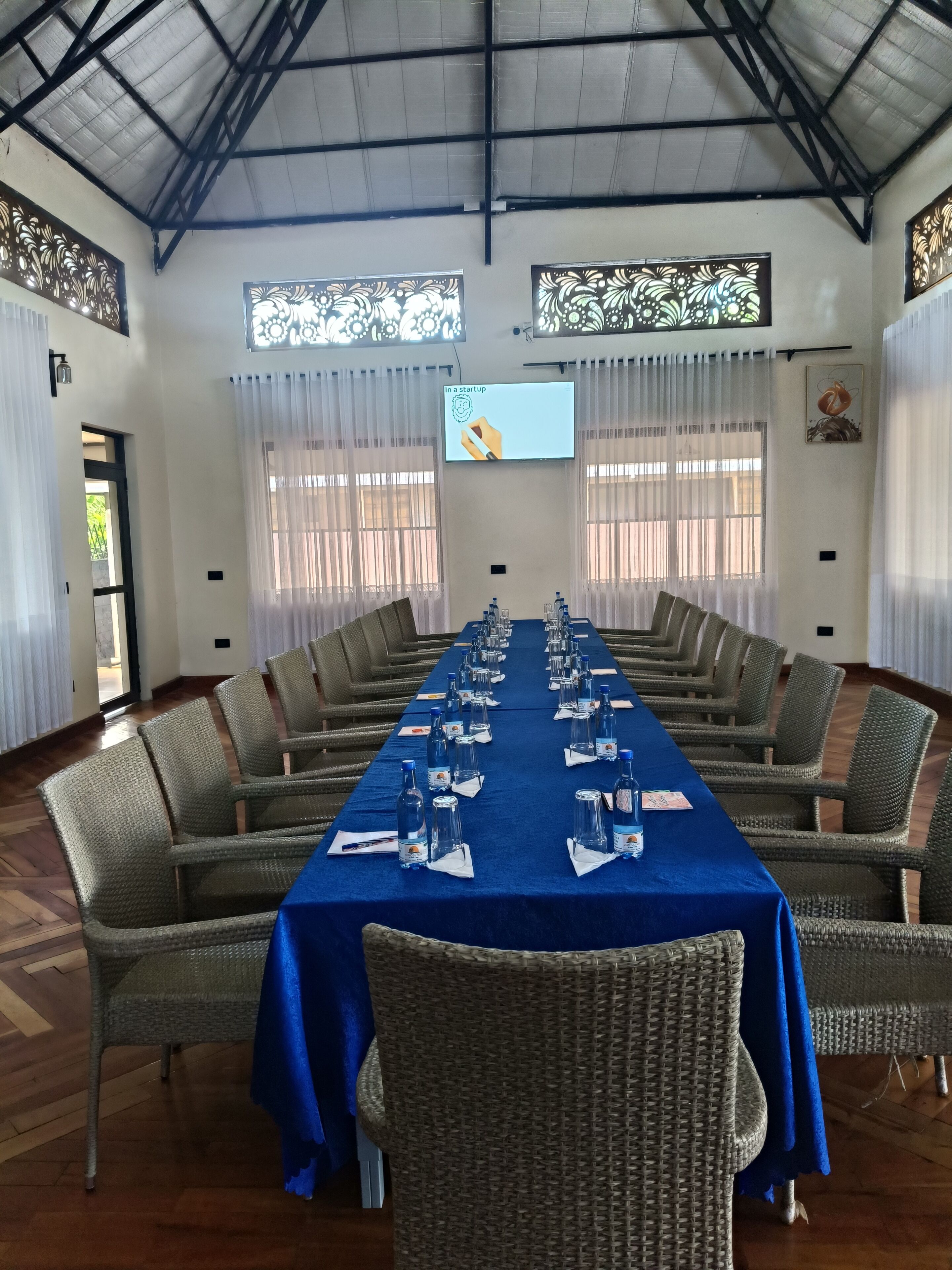 Un salón de conferencias con una larga mesa, sillas de mimbre, un mantel azul y una pantalla mostrando 'In a startup'.