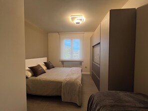 A bedroom with a bed, a window, a radiator, and a wardrobe.