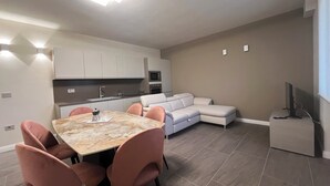 A modern kitchen with white cabinets, a dining table with pink chairs, and a gray sectional sofa. - Cozy suite with contemporary design and comfort for 4 guests Suite Aura (Vernazzano Basso)