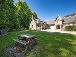 Une maison en pierre avec un garage, une table de pique-nique et une pelouse bien entretenue.