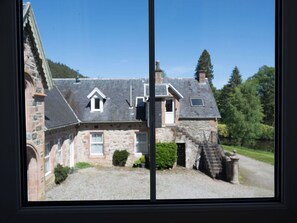 Une maison en pierre avec une allée gravillonnée, un petit jardin et un escalier menant à l’entrée.
